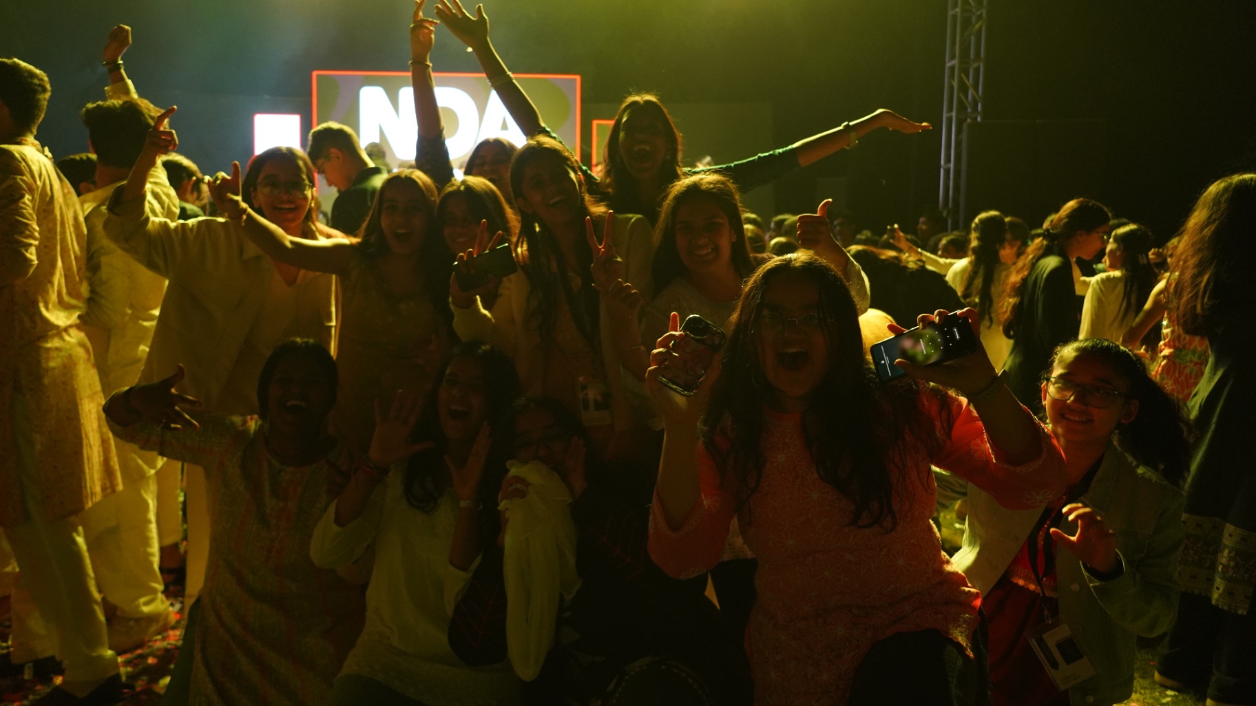 A roaring TMF crowd cheering with hands raised in front of a glowing stage screen at the closing night.